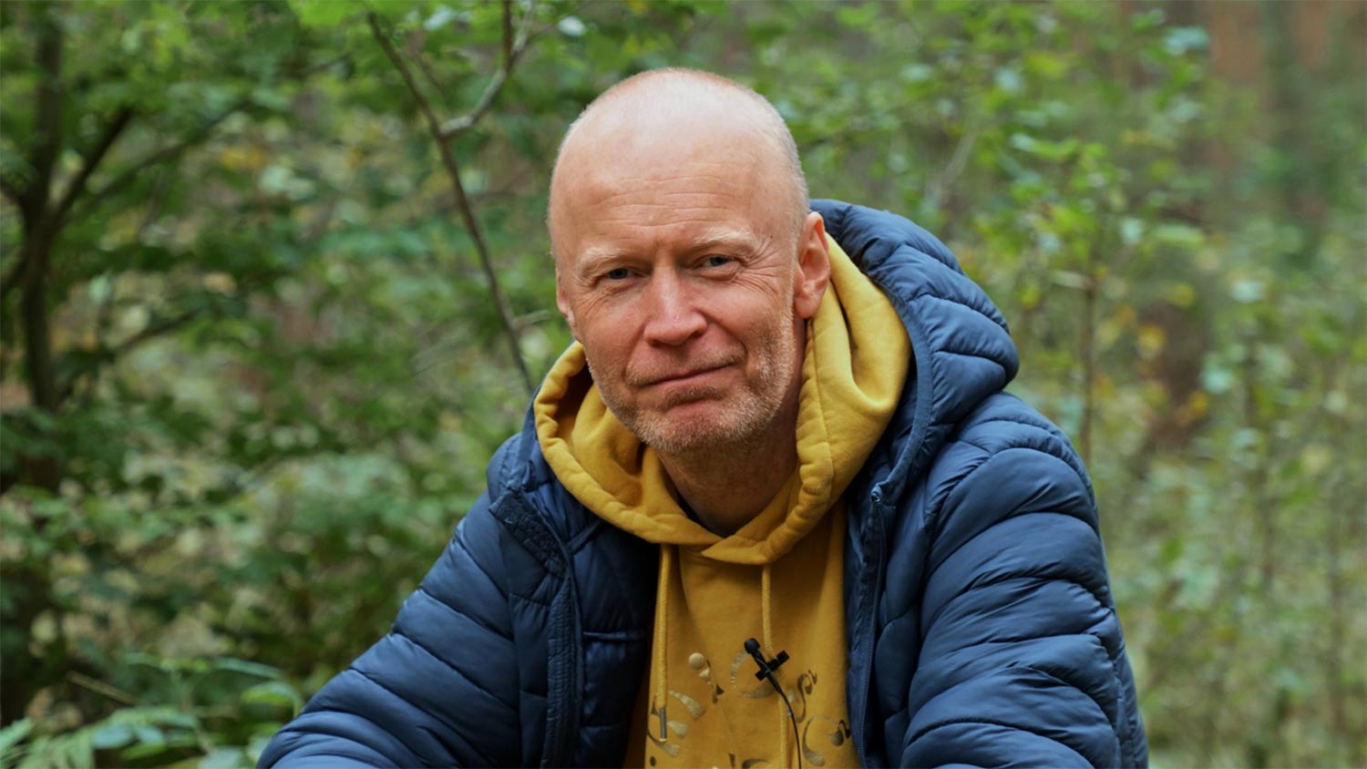 Doświadczony mentor prowadzący warsztaty dla dojrzałych mężczyzn siedzący na trawie i uśmiechający się